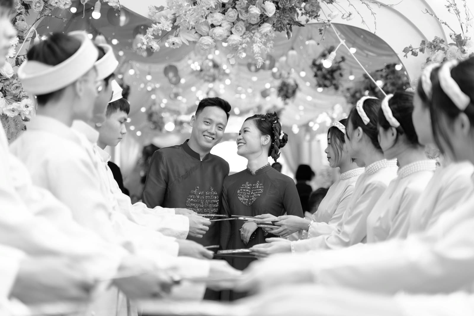 Cô dâu chú rể mặc áo dài cười giữa hai hàng bạn bè áo trắng