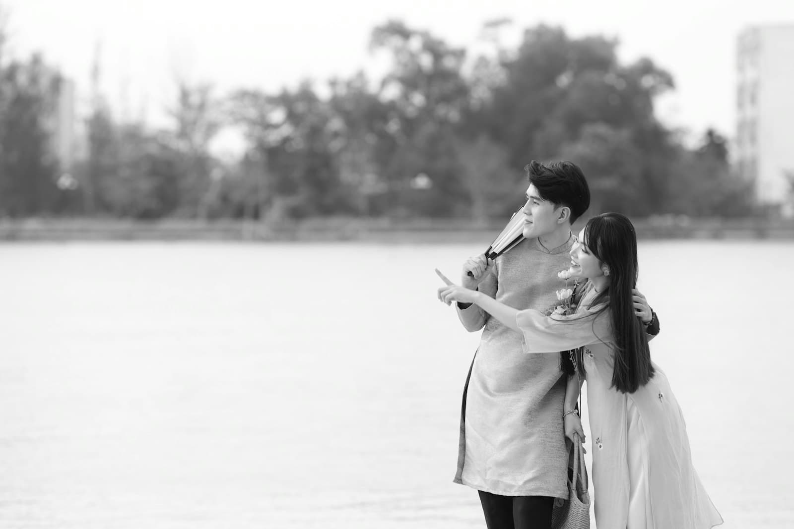 Cặp đôi đùa vui bên mặt hồ rộng, xa xa là hàng cây