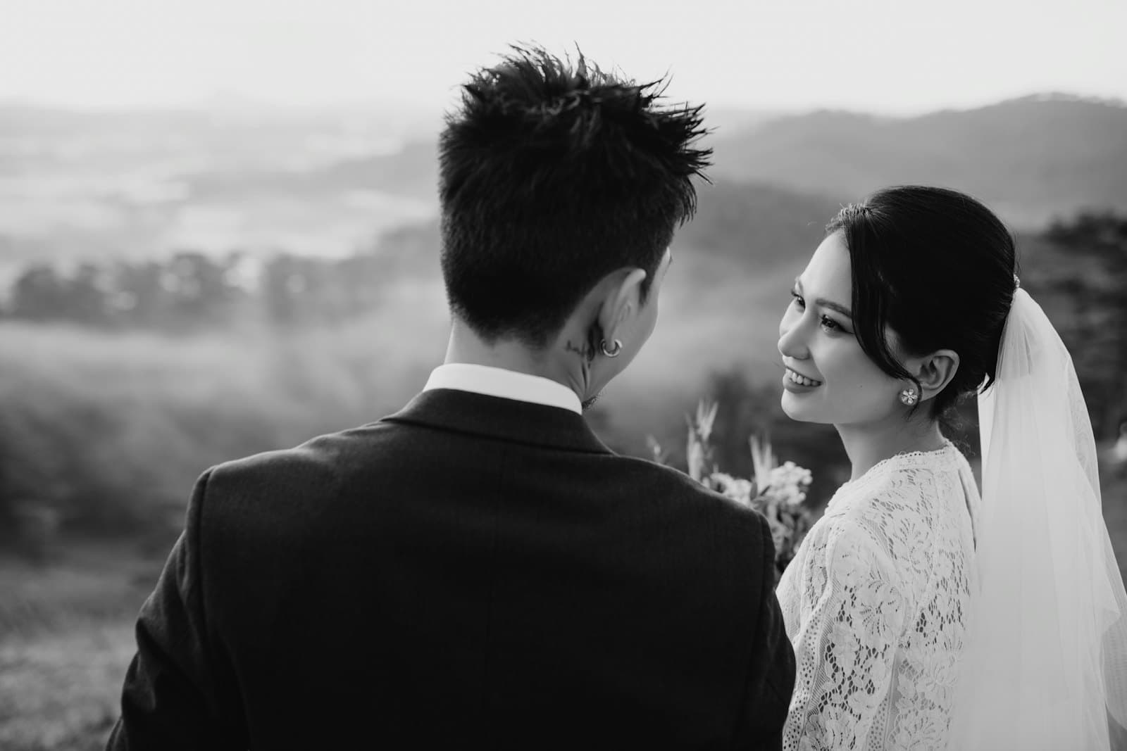 Cô dâu nhìn chú rể, phía sau là đồi núi mờ sương